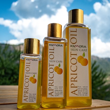 Three bottles of different sizes of Kilmora's cold pressed apricot oil in the foreground. With blue skies and some clouds showing at the back