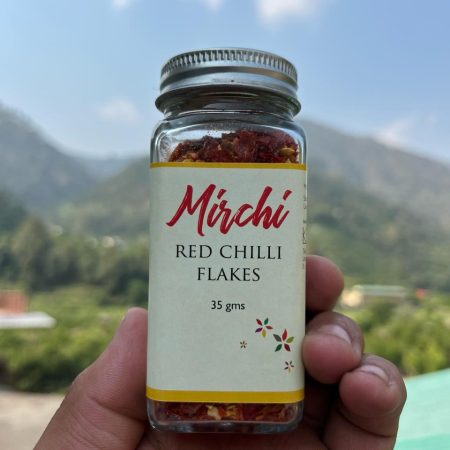 Glass jar with Chilli flakes printed on it. Held up against the sky.