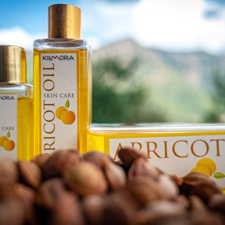 Image shows apricot kernels in foreground with three apricot oil bottles of different sizes behind the kernels
