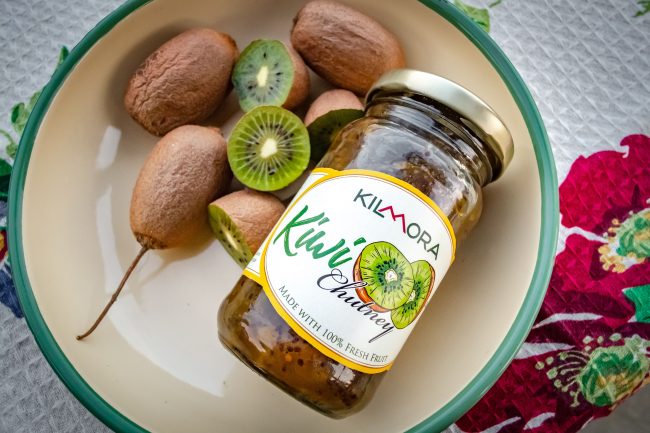 Jar of Kilmora Kiwi Chutney ket next to ripe kiwi fruits with two halves of kiwi fruits also shown
