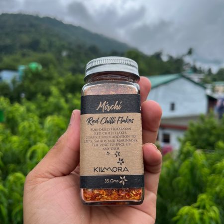Glass jar with Chilli flakes printed on it. Held up against the sky.