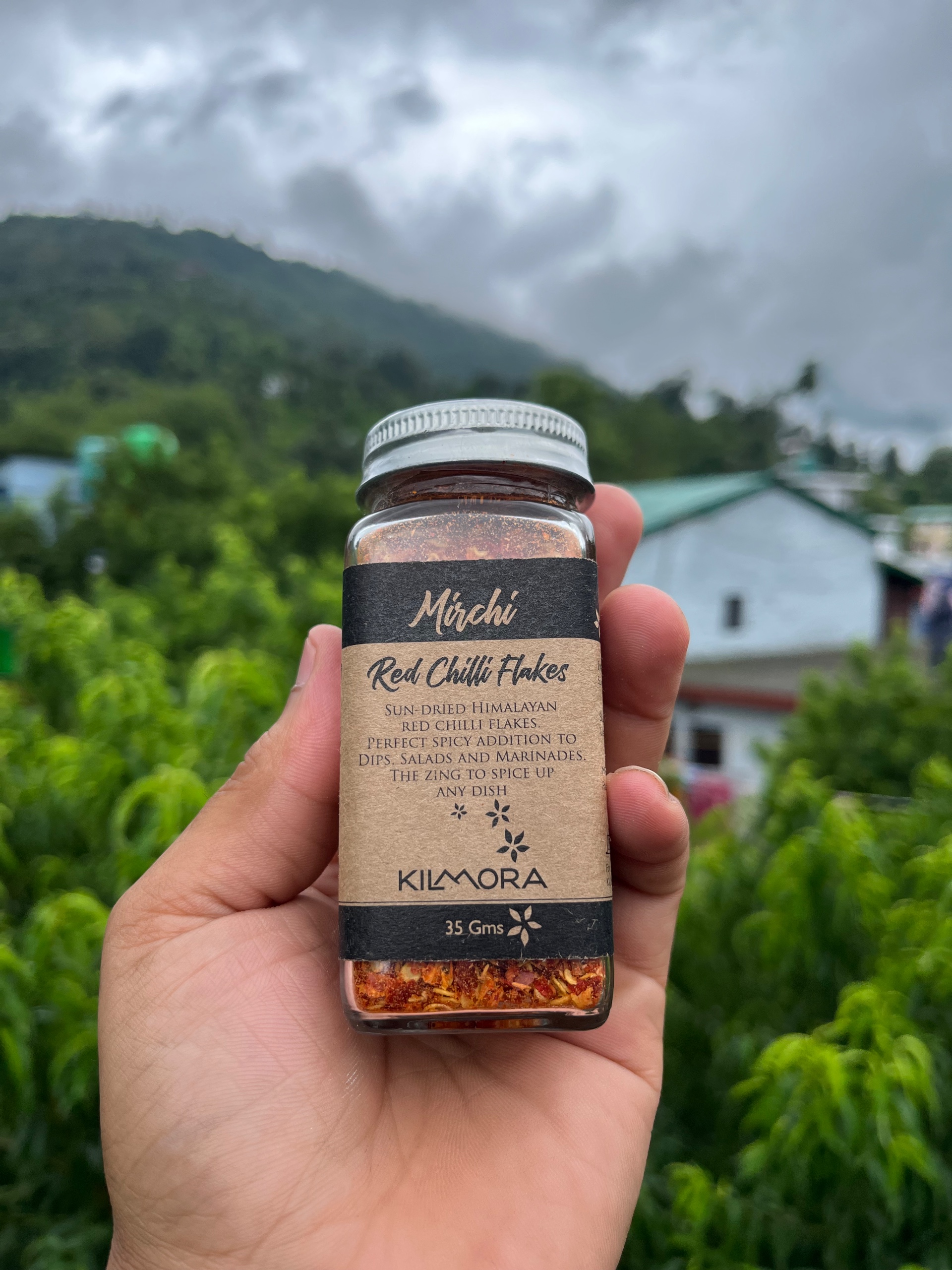 Glass jar with Chilli flakes printed on it. Held up against the sky.