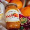 Jar of Malta Marmalade lying atop floral cloth napkin with some Malta fruits in the background