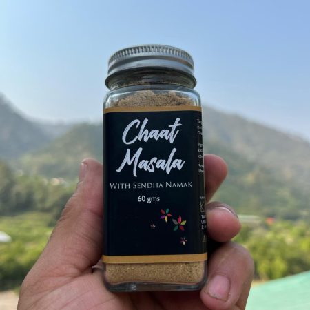 Glass jar with Chaat Masala with sendha namak printed on it. Held up against the sky.