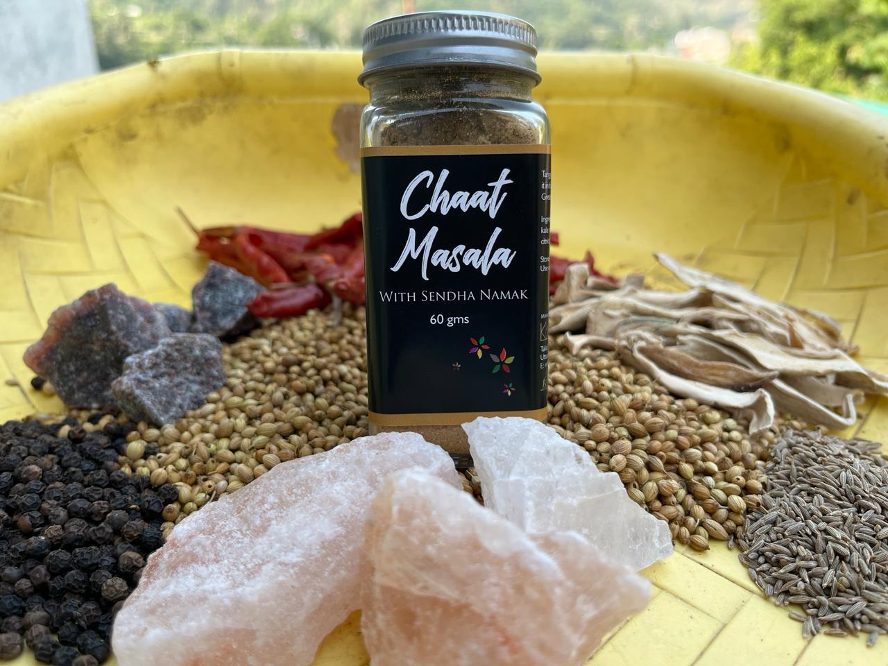 Glass jar with Chaat Masala with sendha namal printed on it. Surrounded with the raw ingredients which are used to make this blend.