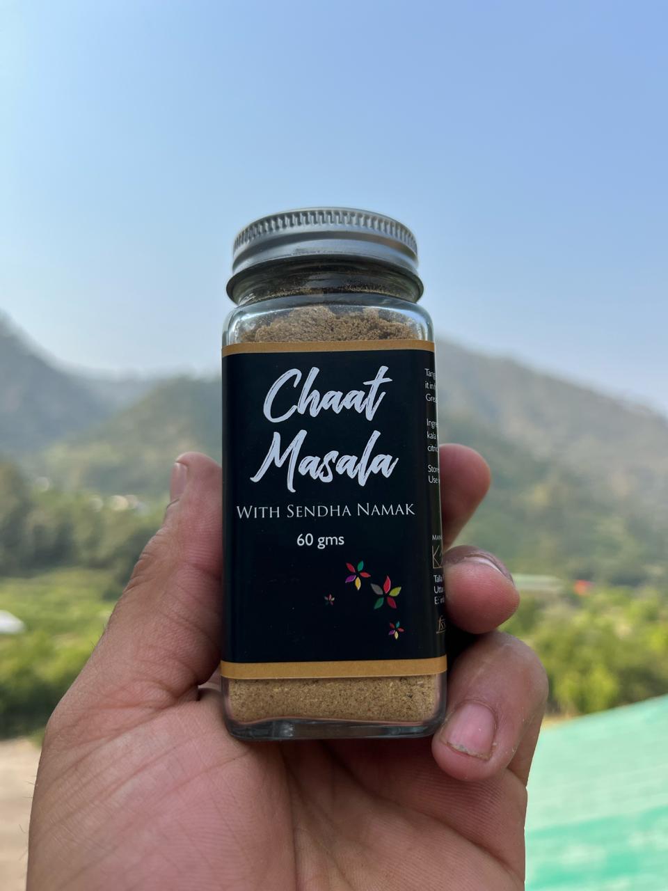 Glass jar with Chaat Masala with sendha namak printed on it. Held up against the sky.