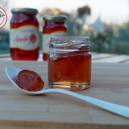 White spoon with apple jelly in the foreground with two jars of apple jelly in the background