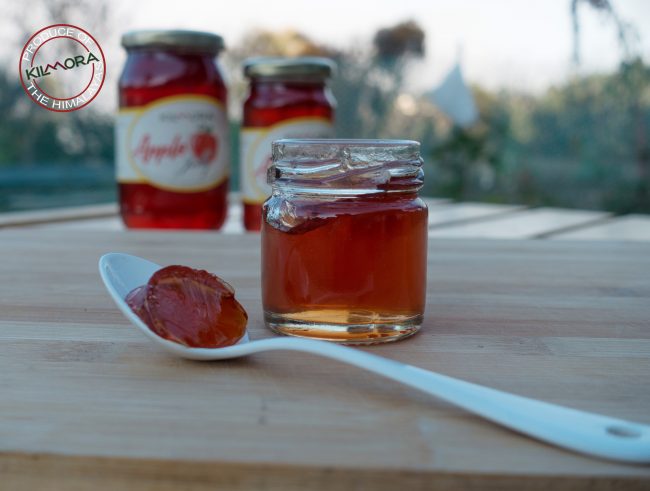White spoon with apple jelly in the foreground with two jars of apple jelly in the background
