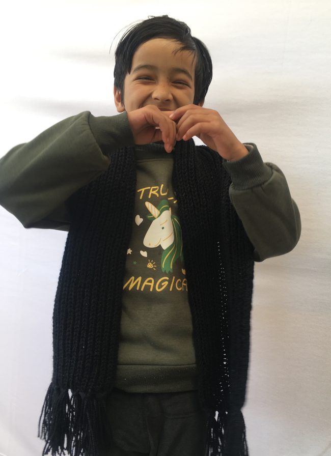 Child showing a black hand knitted muffler and laughing