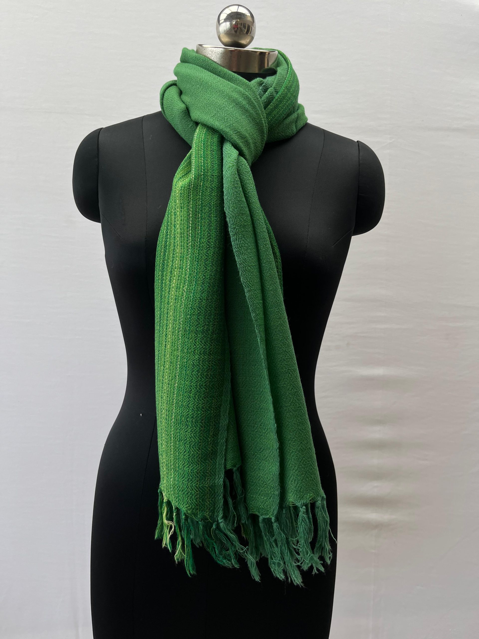 Merino wool stole knotted on a mannequin. Handwoven in fern green with a vertical border on one side