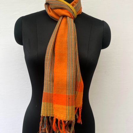 Merino wool scarf with an orange border on one side and an ochre yellow one on the other. With thin pin stripes in deep forest green in between on an ochre yellow background.