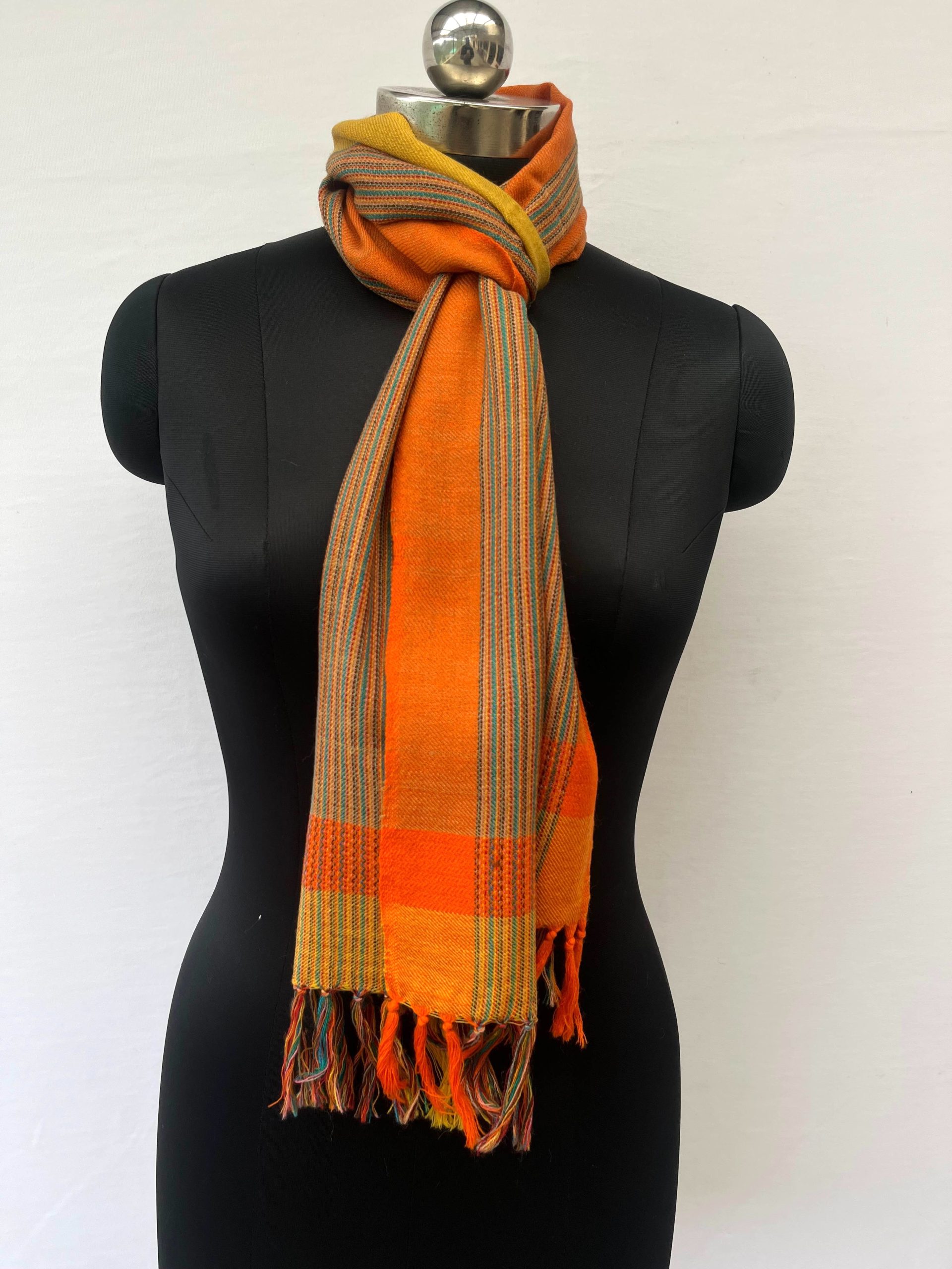 Merino wool scarf with an orange border on one side and an ochre yellow one on the other. With thin pin stripes in deep forest green in between on an ochre yellow background.