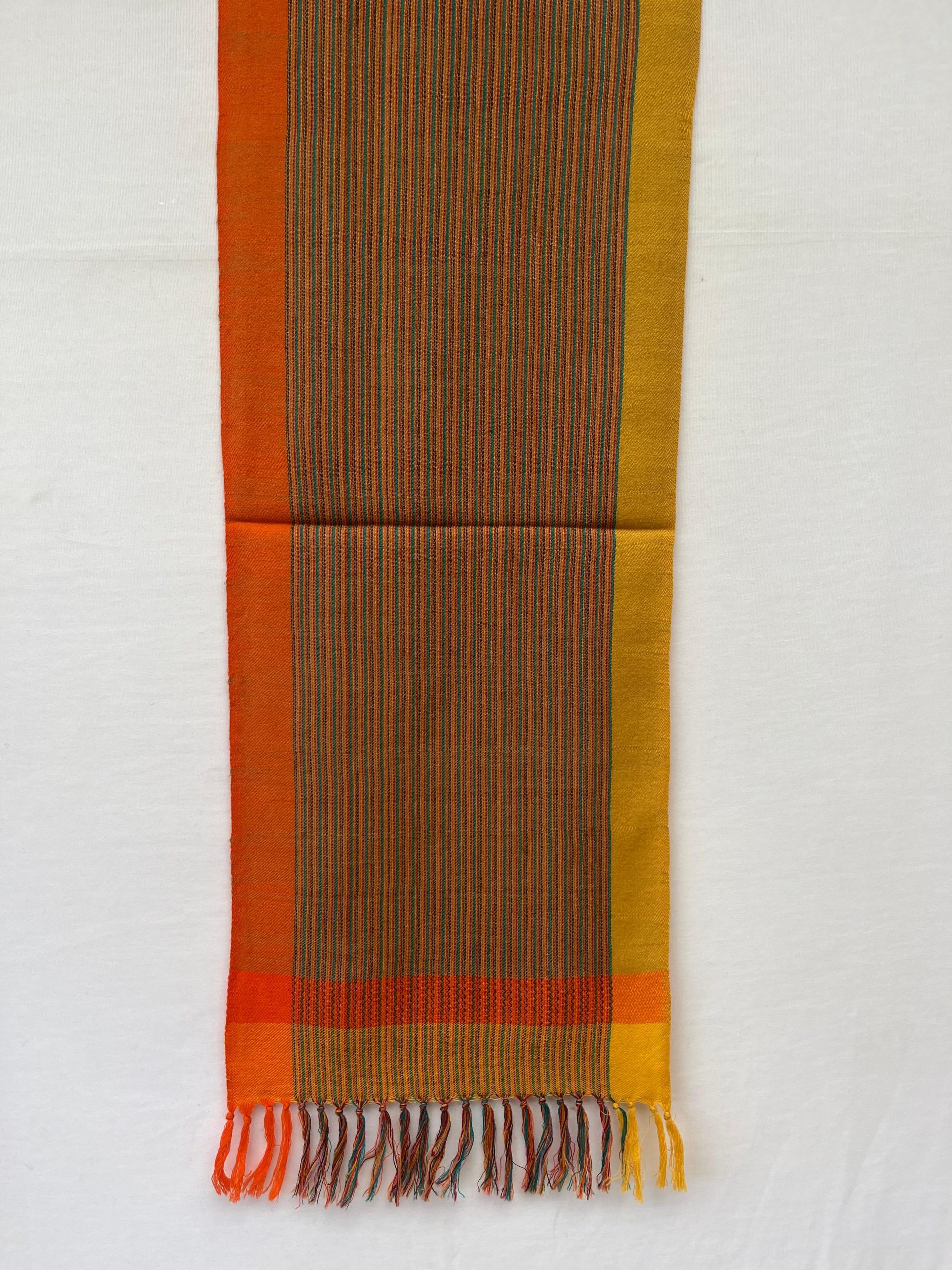 Merino wool scarf with an orange border on one side and an ochre yellow one on the other. With thin pin stripes in deep forest green in between on an ochre yellow background.