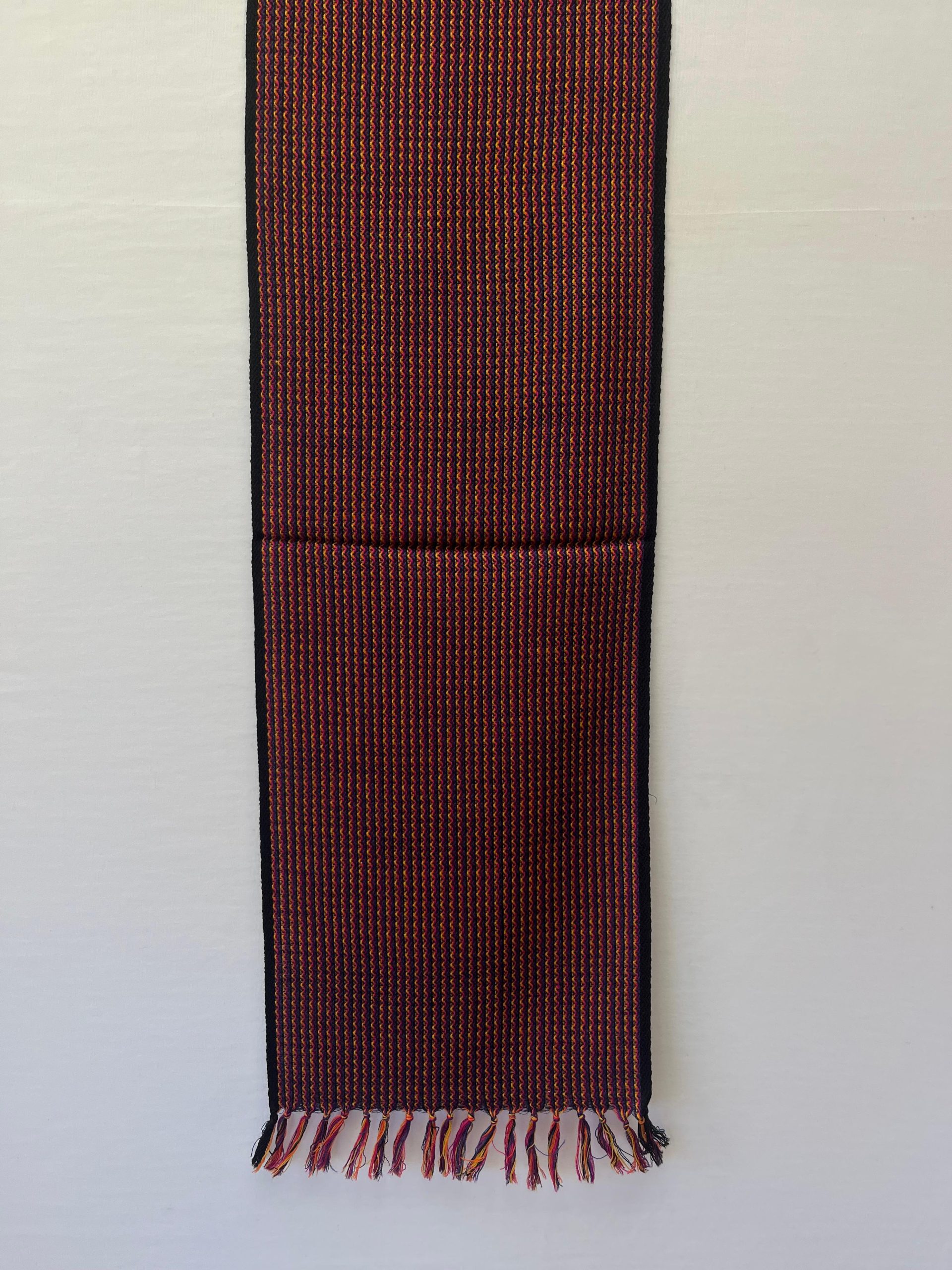 Handwoven merino wool scarf in wavy striped pattern of reds, browns and yellows with a deep brown selvedge
