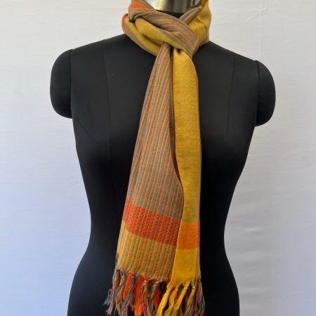 Merino wool scarf with an orange border on one side and an ochre yellow one on the other. With thin pin stripes in deep forest green in between on an ochre yellow background.