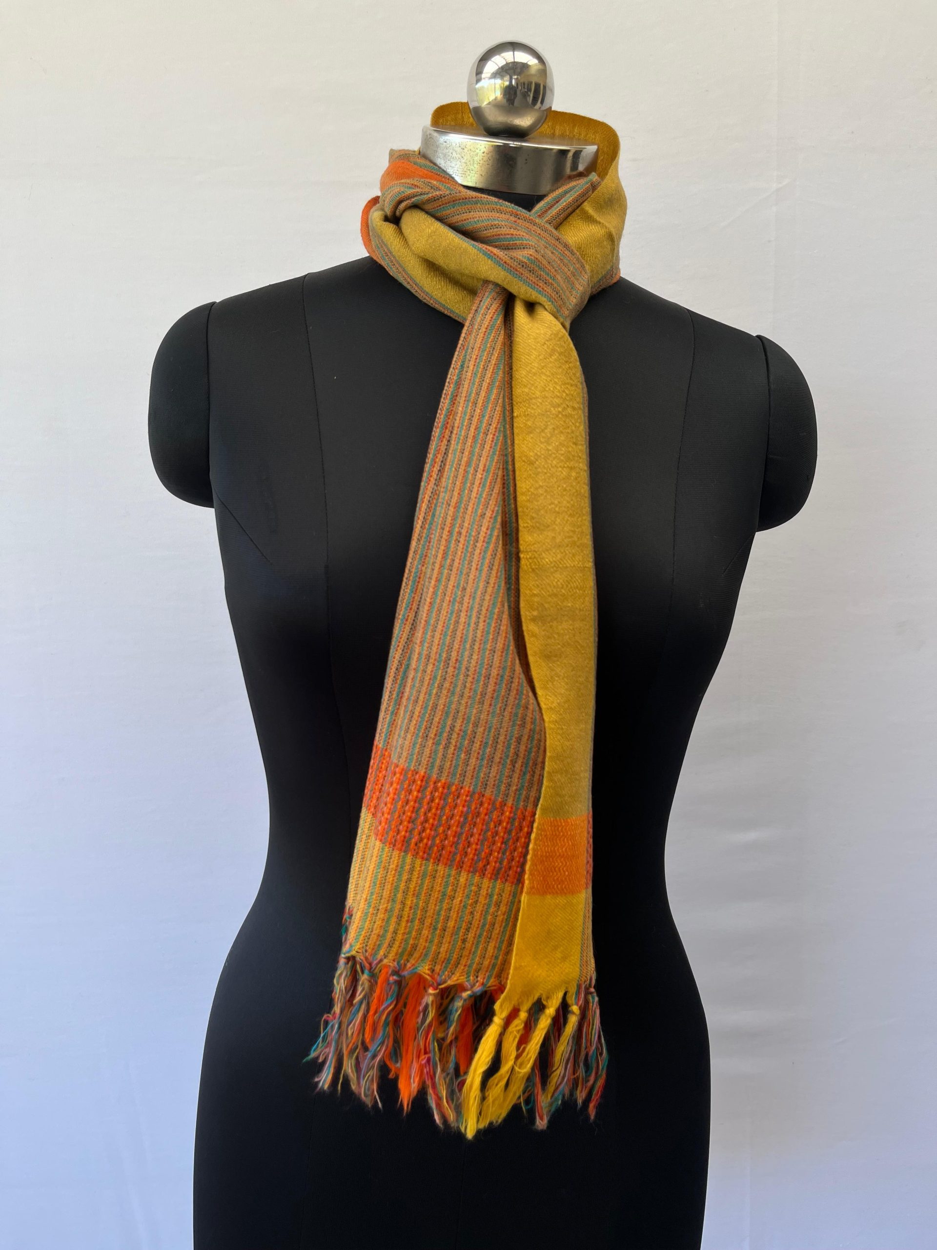 Merino wool scarf with an orange border on one side and an ochre yellow one on the other. With thin pin stripes in deep forest green in between on an ochre yellow background.
