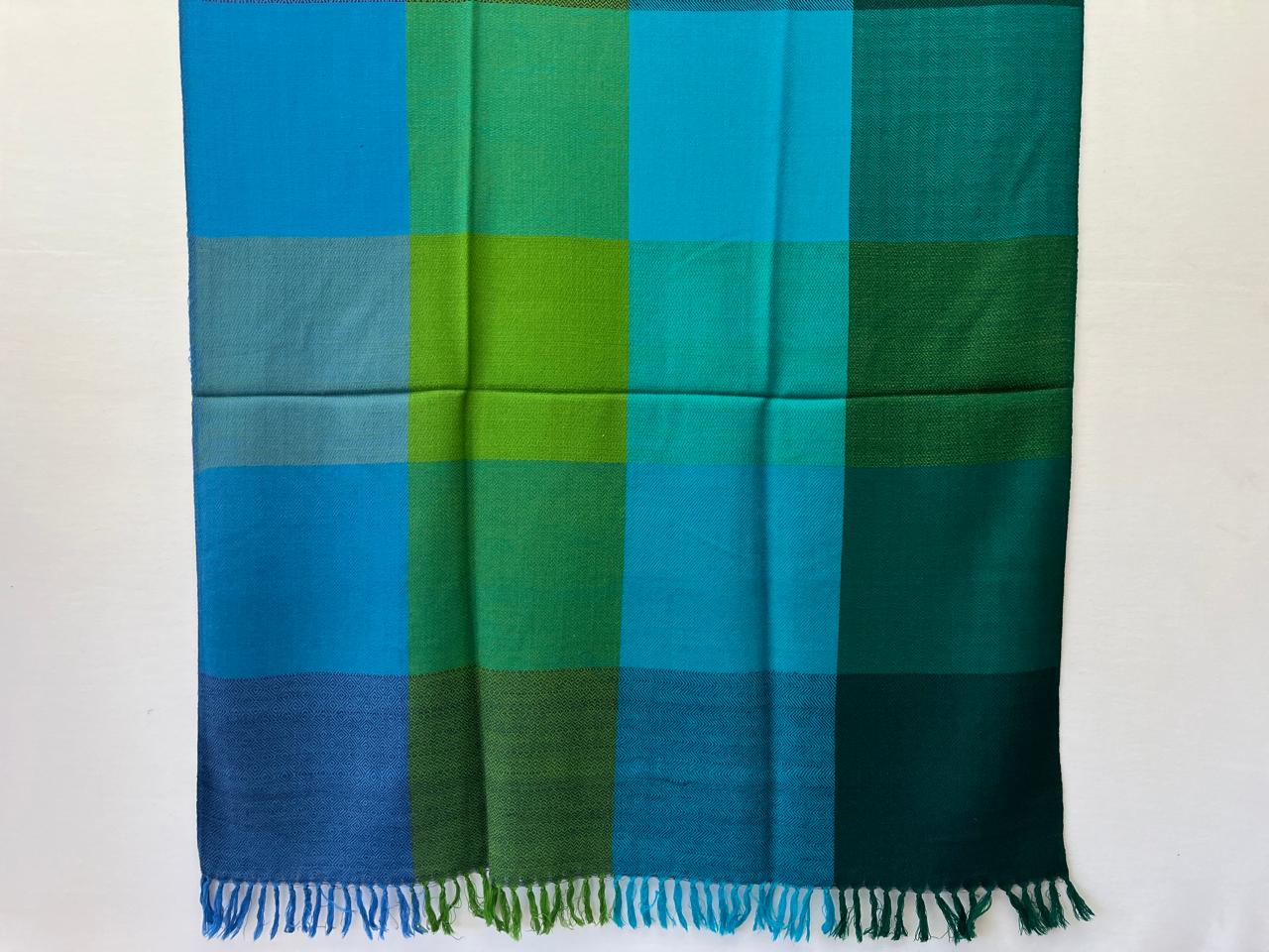 Hand-woven merino wool in large bold checks in 4 panels - left to right - panels of checks of cerulean and sky, then panels of emeral and jade green, followed by panels of sapphire, teal and sky, and lastly panel with bold checks in pine, juniper and moss green