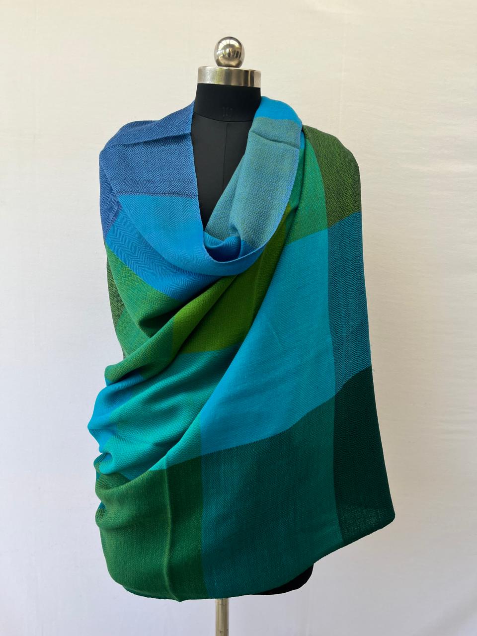 Mannequin with a hand-woven merino wool draped. In large bold checks in 4 panels - left to right - panels of checks of cerulean and sky, then panels of emeral and jade green, followed by panels of sapphire, teal and sky, and lastly panel with bold checks in pine, juniper and moss green