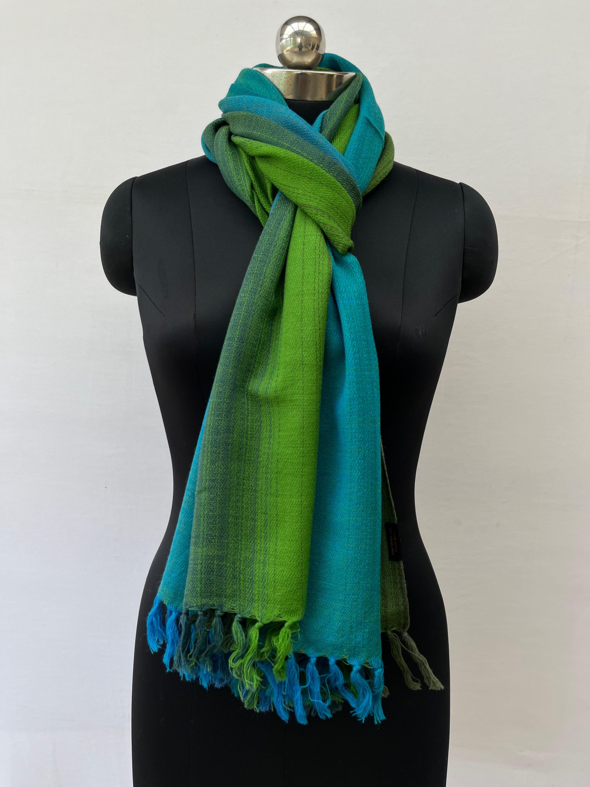 Ombre hand woven merino wool stole in gradation of teal blue, deep cerulean, burdock green and pine. Knotted on a mannequin.