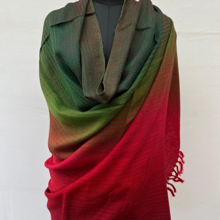 Ombre hand woven merino wool shawl in shades that start with a deep pine green on the left and end with deep maroon on the right. Draped on a mannequin.