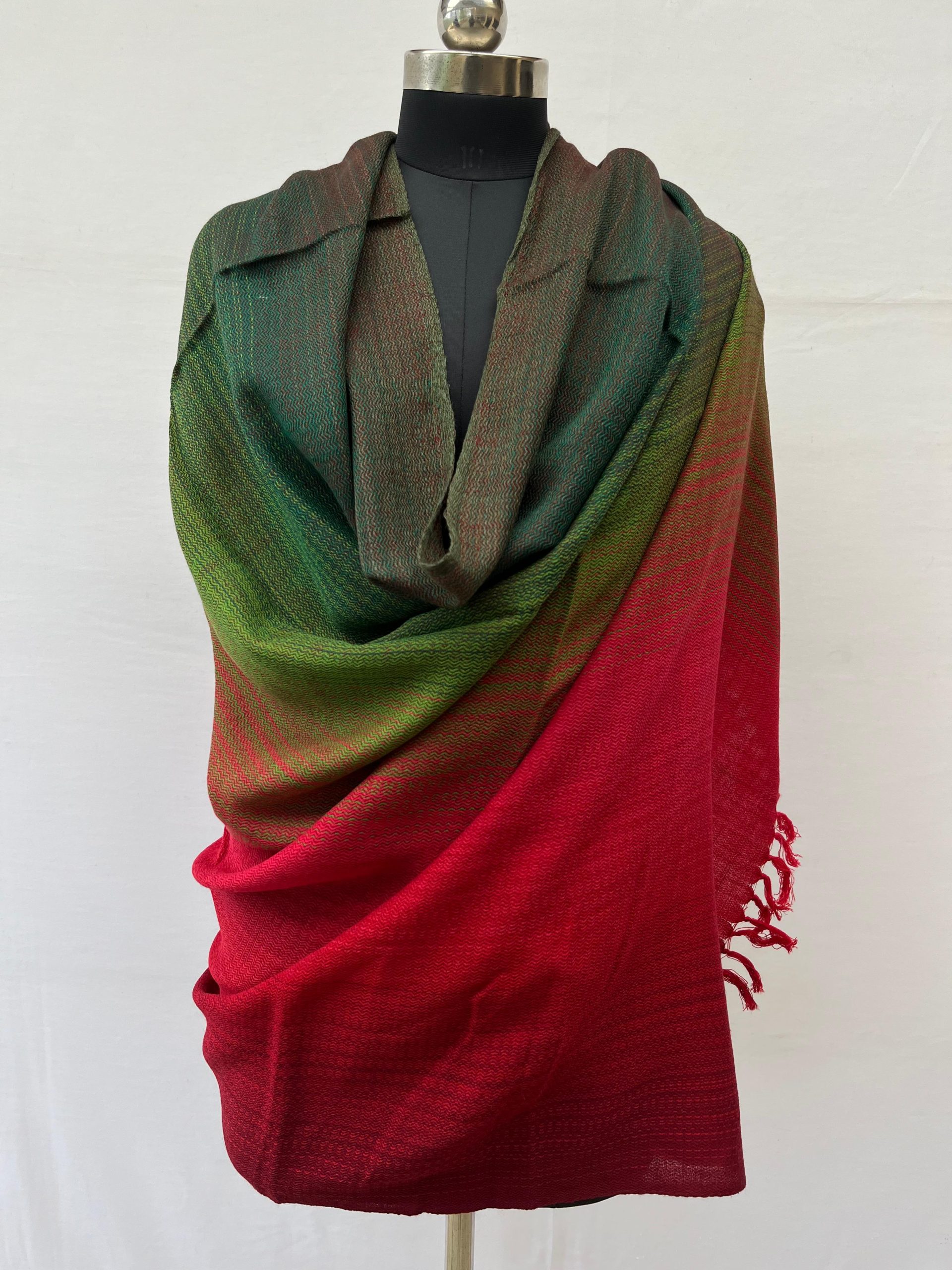 Ombre hand woven merino wool shawl in shades that start with a deep pine green on the left and end with deep maroon on the right. Draped on a mannequin.