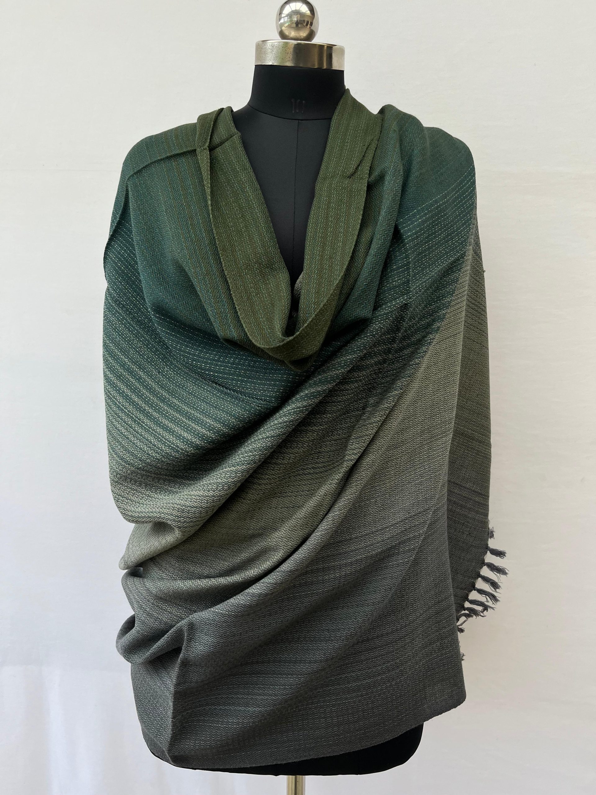 Hand woven merino wool ombre shawl in shades of deep pine green, moss green, solver and pewter. Draped ona mannequin.
