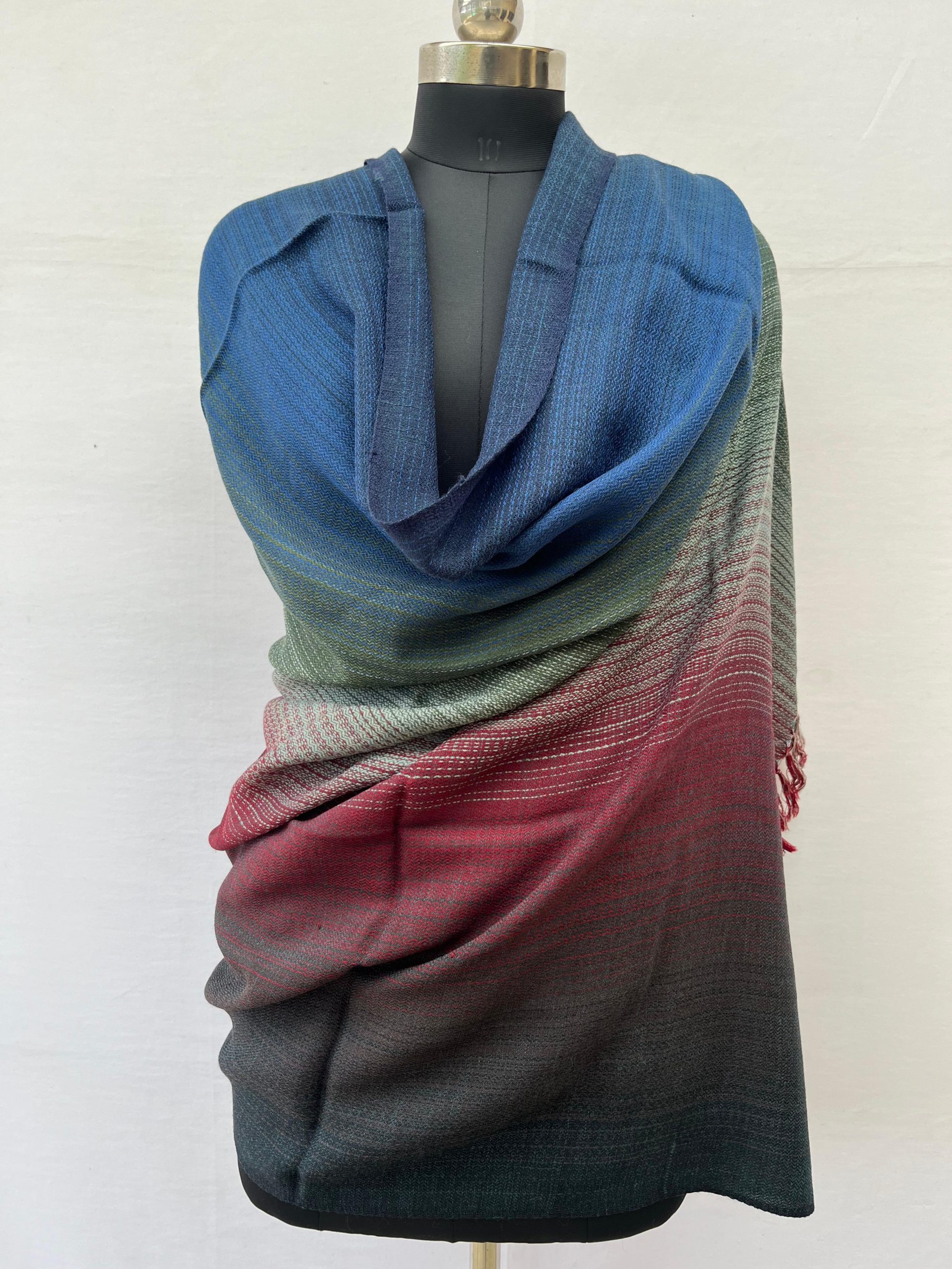 Ombre hand woven merino wool shawl. Starting with deep wine red, graduating to amethyst, silver, graphite and deep blue. Draped on a mannequin.