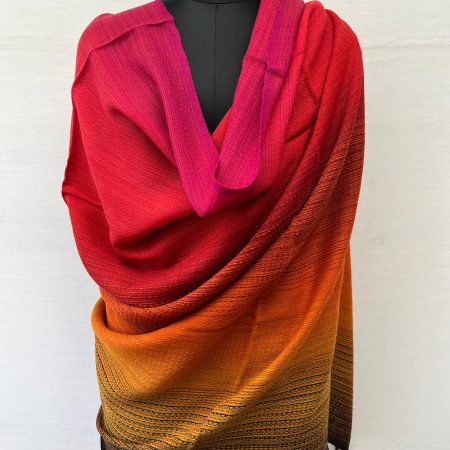 Ombre hand woven merino wool shawl in shades starting with deep red, scarlet, orange and ending with hint of pine green. Draped on a mannequin.