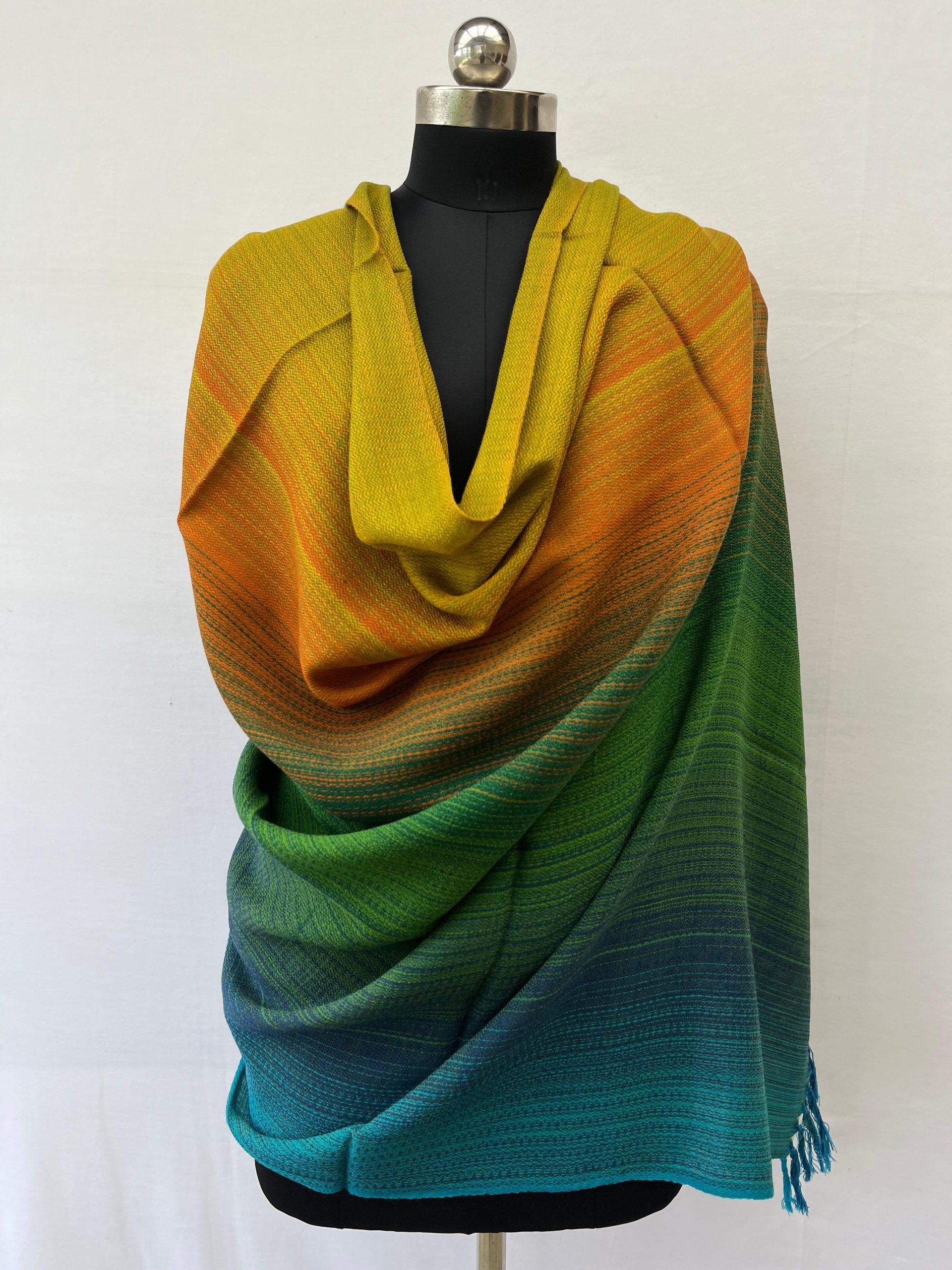 Ombre handwoven merino wool shawl in shades ranging from forest green, pine green, marigold to ochre. Here, draped on a mannequin.