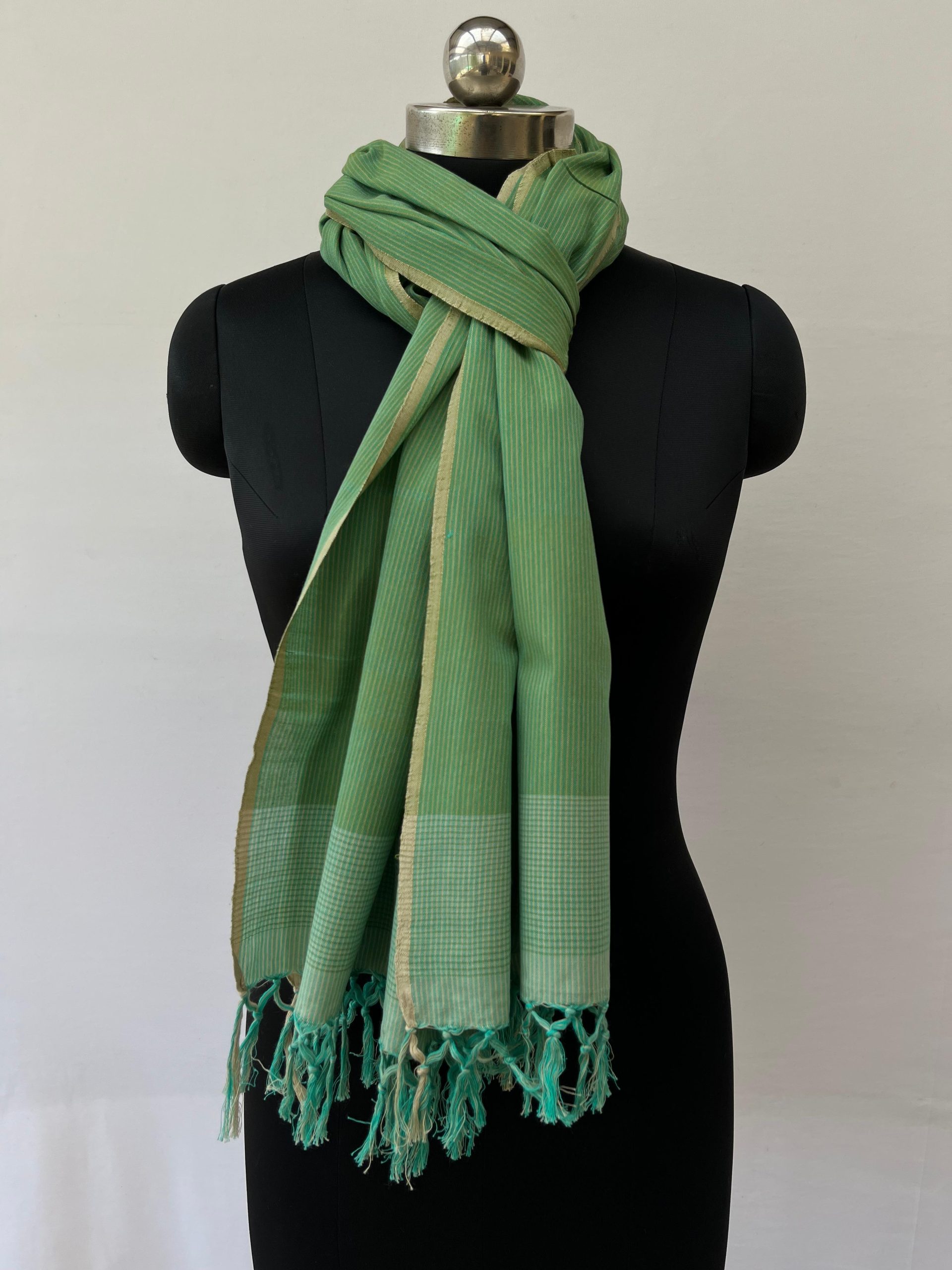 Hand woven cotton stole in pistachio green with an overlay of sage green and thin vertical pin stripes for design, Knotted on a mannequin.
