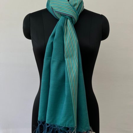 Hand-woven cotton stole in a deep teal with a striped teal and sea foam green vertical border on one side of the stole. Knotted on a mannequin.