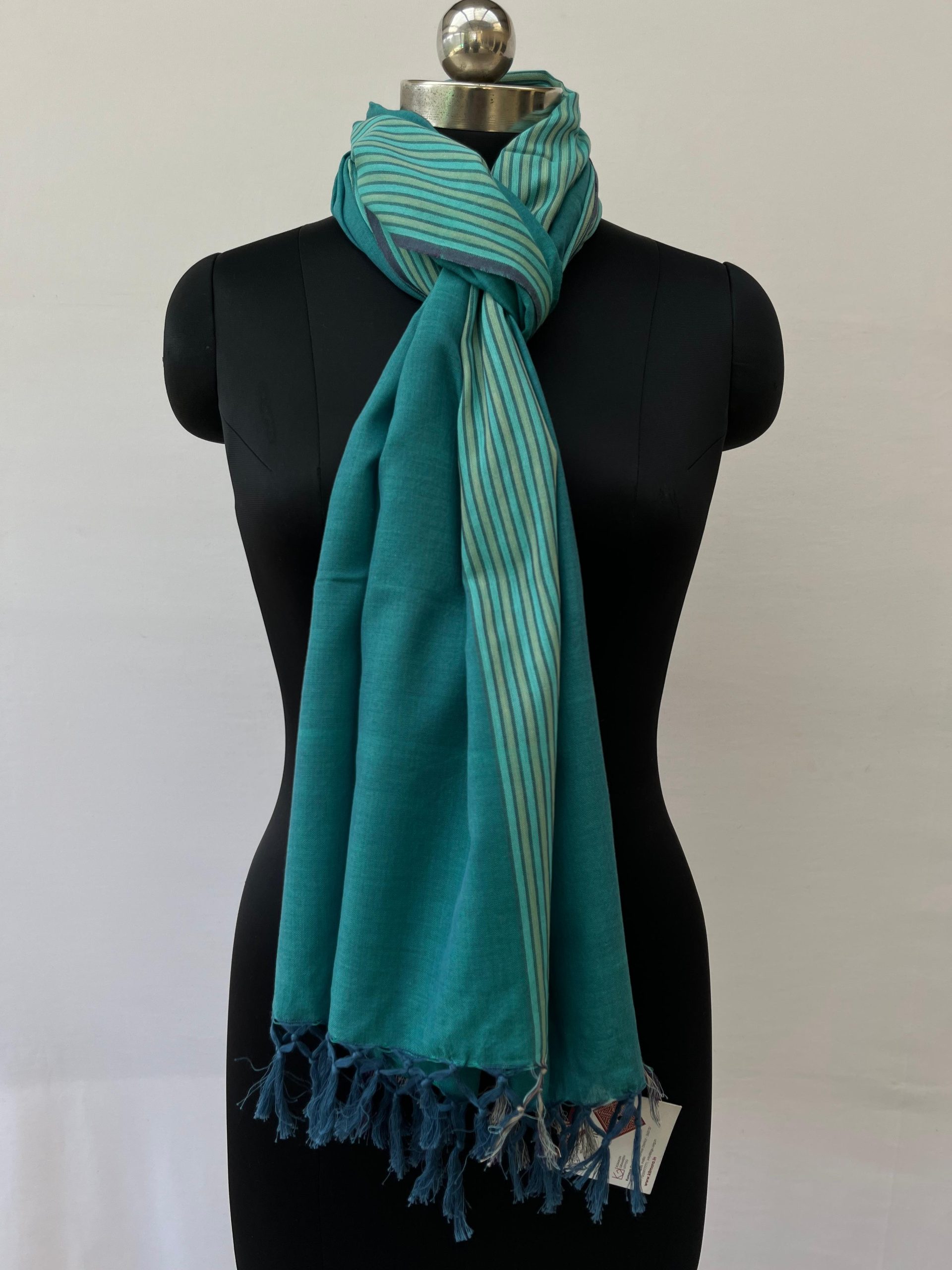 Hand-woven cotton stole in a deep teal with a striped teal and sea foam green vertical border on one side of the stole. Knotted on a mannequin.