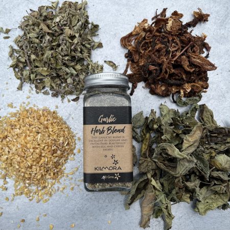 A flat lay photograph of a jar in the center with a Kraft paper label saying Garlic Herb Blend. With sun-dried garlic flakes, oregano, dried onion slices and basil placed in a circle around it.