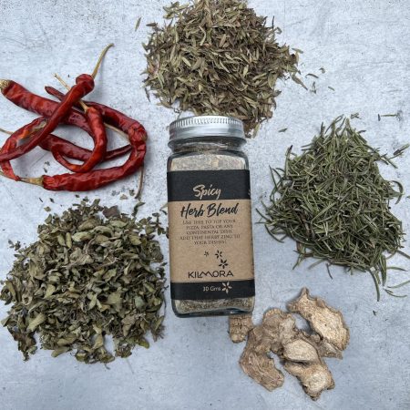 A flat lay photograph of a jar in the center with a Kraft paper label saying Spicy Herb Blend. With dry red chillies, oregano, dry ginger slices and thyme placed in a circle around it.