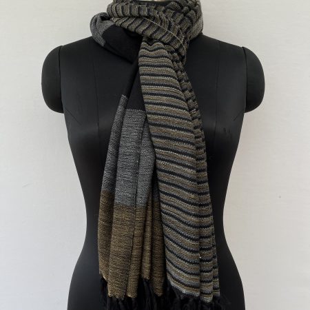 Hand-woven merino wool stole with two different halves to the stole. One half has thin vertical stripes in mustard, silver gray and black. The other half with large vertical stripes of mustard, silver gray and black.